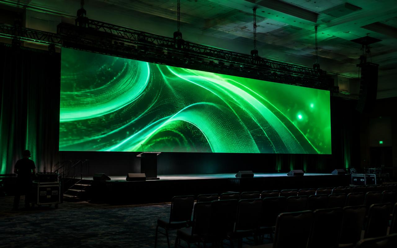 Hung LED video wall suspended from black truss and chain hoists behind a keynote stage in a ballroom
